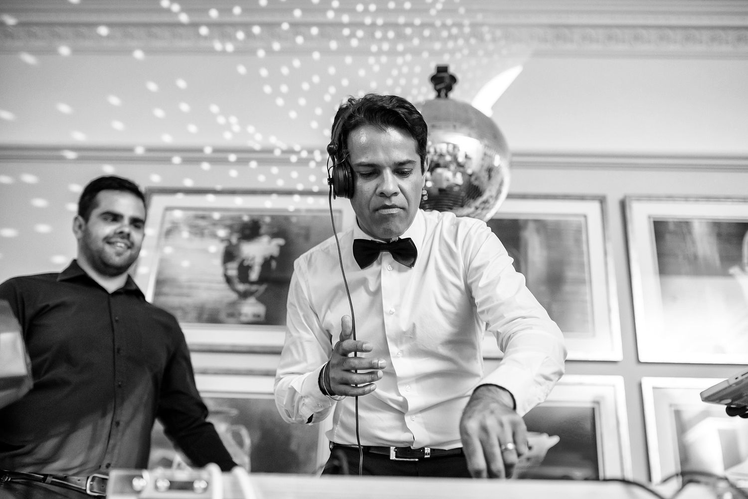 Black and white photo of guests mingling at wedding reception under twinkling ceiling lights.