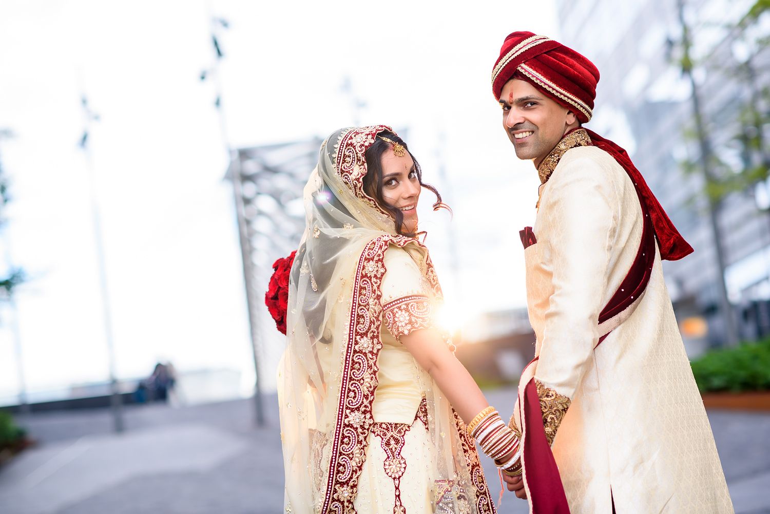 Romantic wedding portrait with couple in traditional Indian attire against modern architecture.