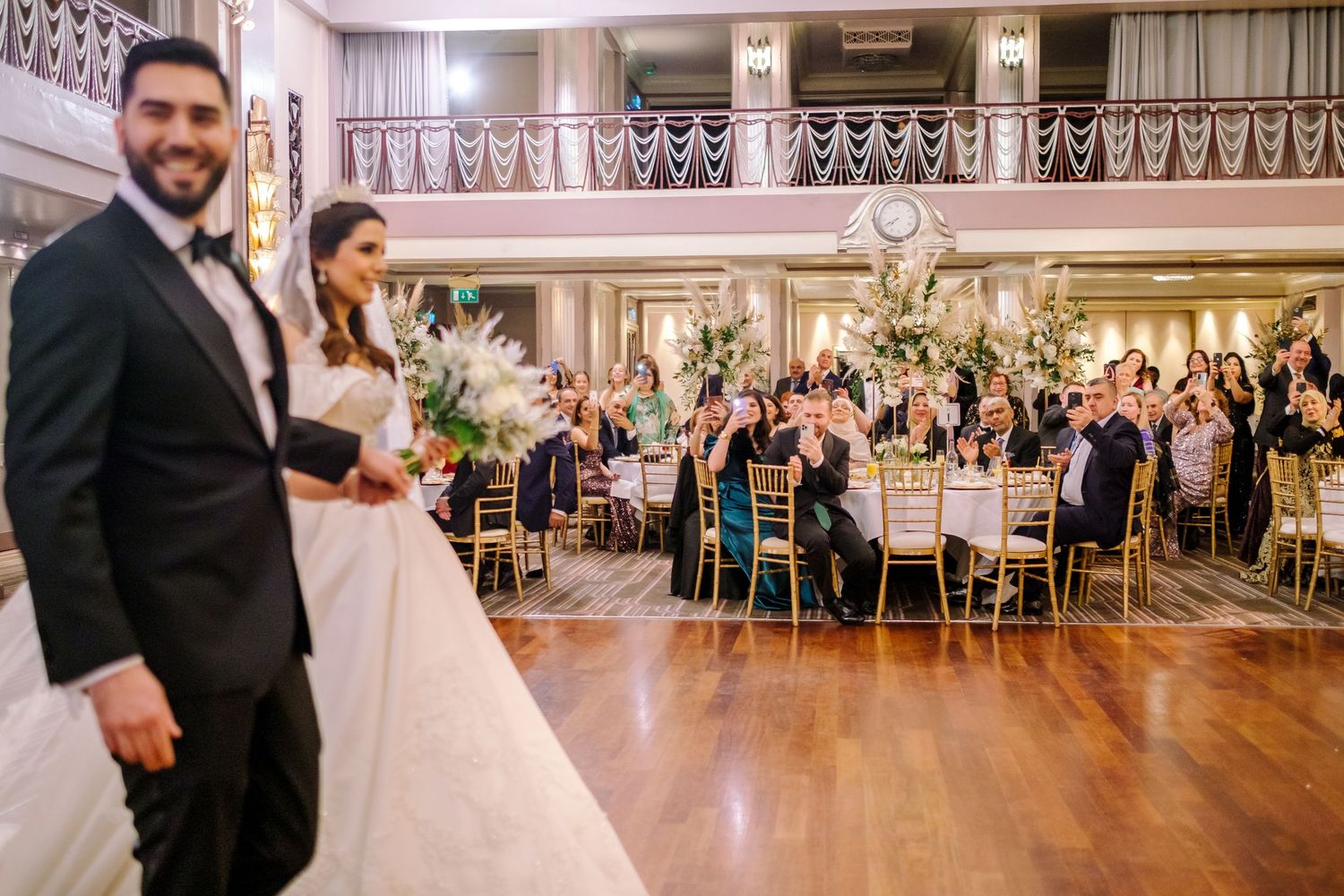 Wedding guests dancing and celebrating in an elegant ballroom with ornate decor and lighting.