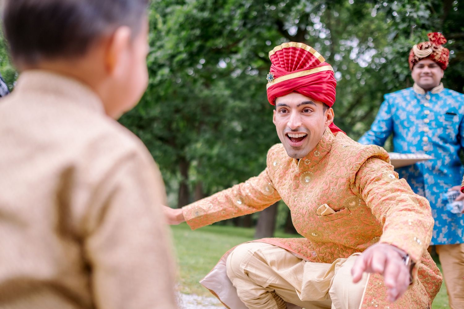 Wedding guest in orange sherwani and red turban shares joyful moment during outdoor celebration.
