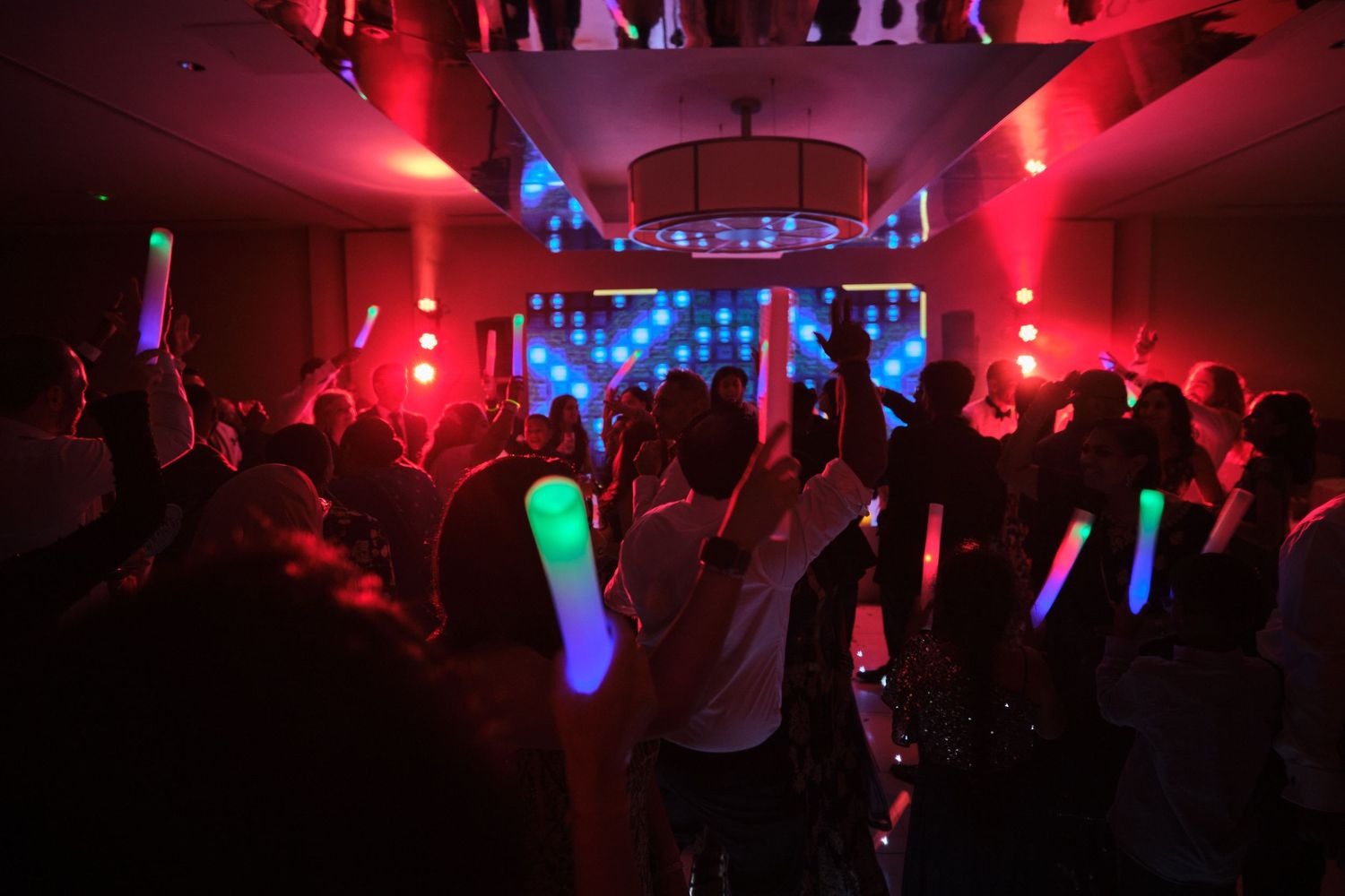 Dance floor illuminated with red and blue lights as party guests celebrate with glowing LED wands.