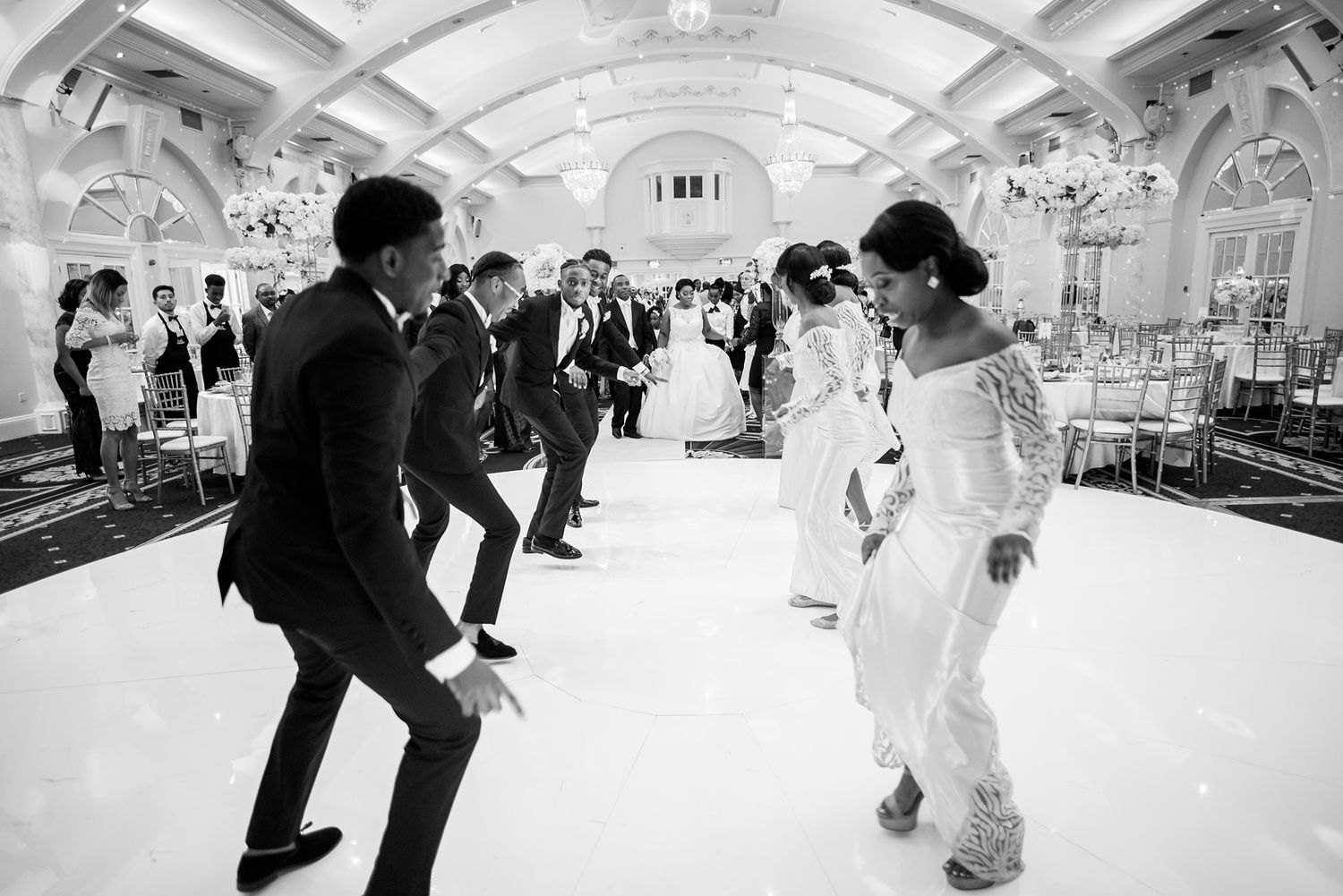 Wedding party dancing and celebrating in an ornate ballroom venue.