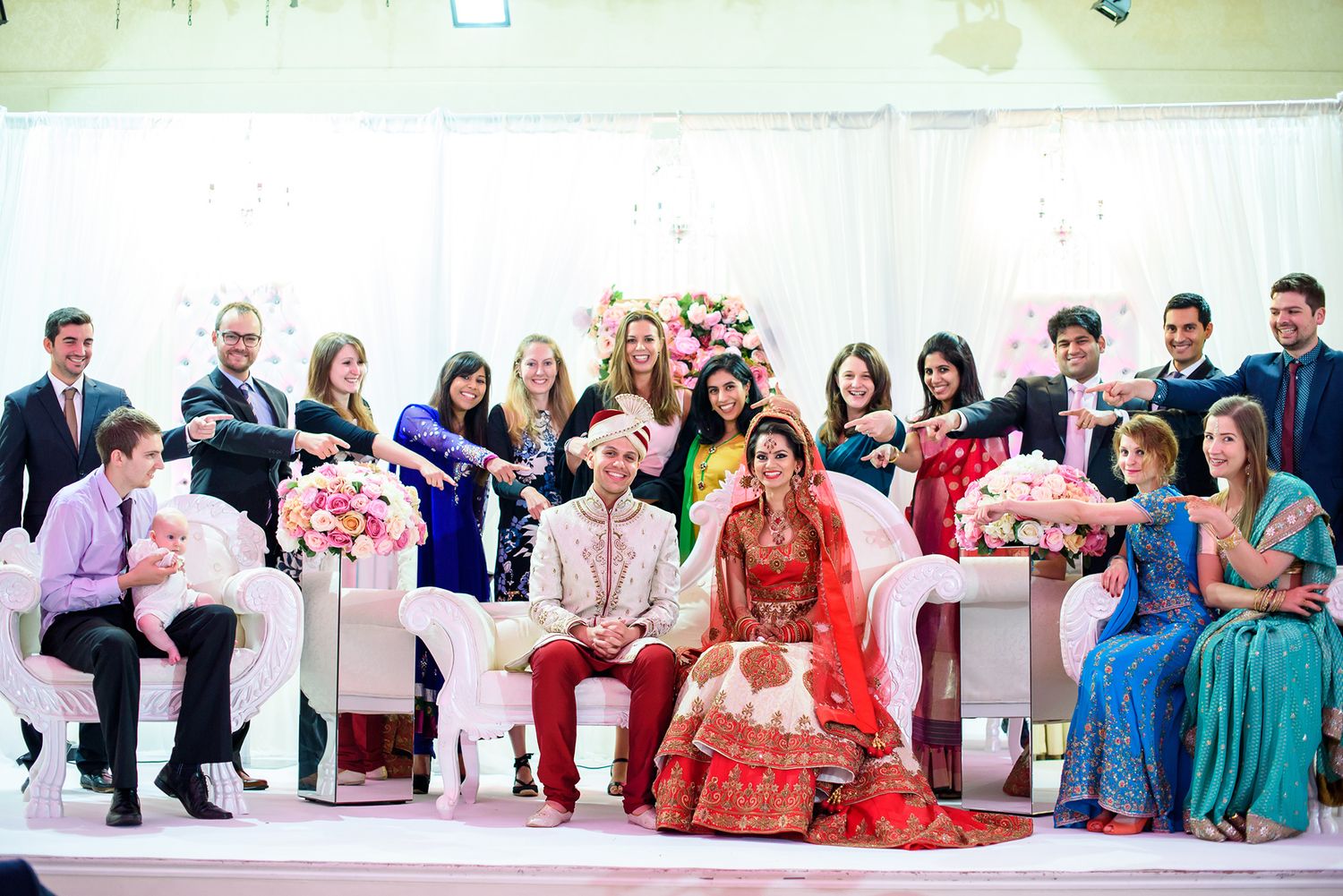 Wedding guests gathered in formal attire watching a cultural ceremony at an indoor venue.