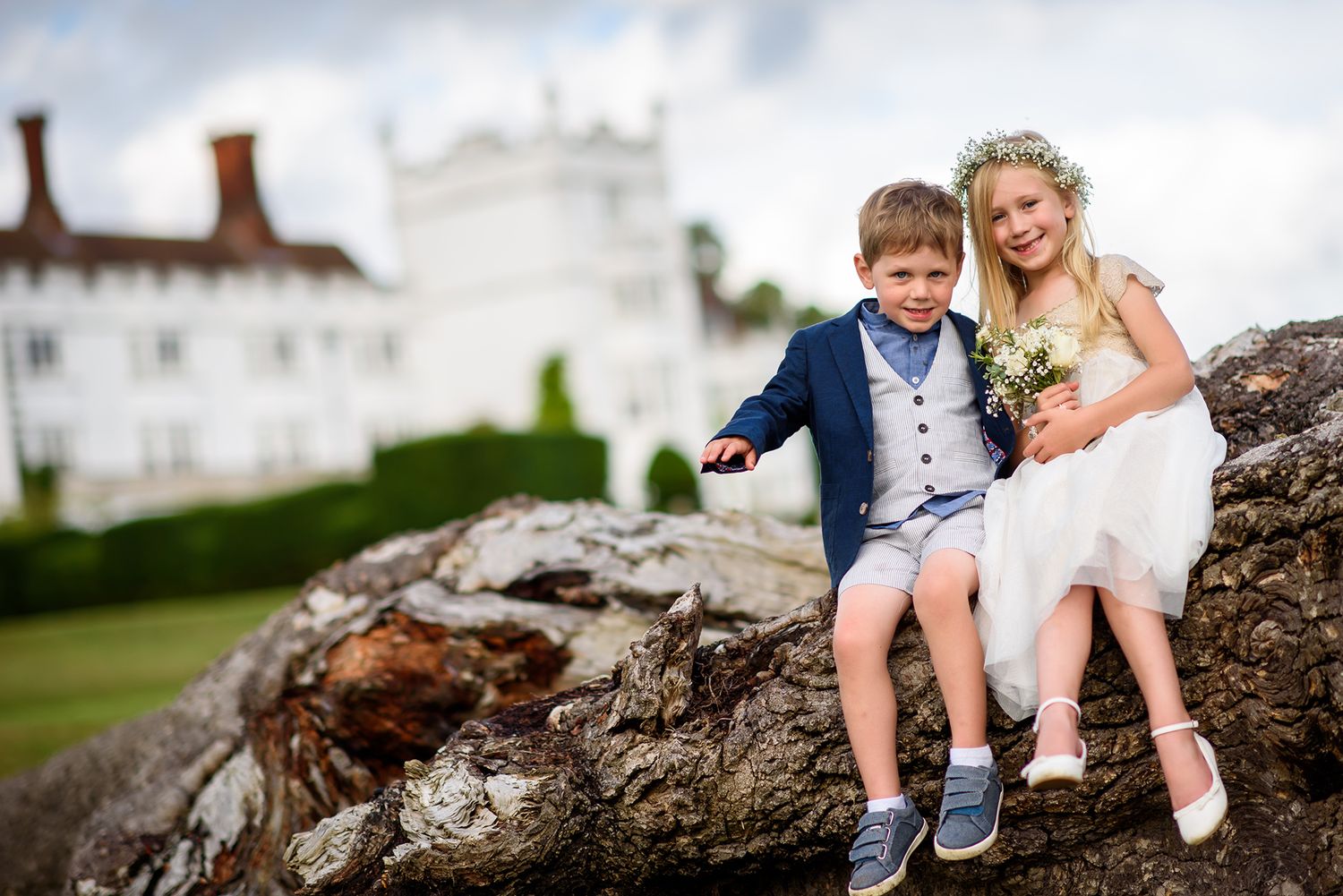 Children and adults gather on fallen tree trunk during outdoor wedding.