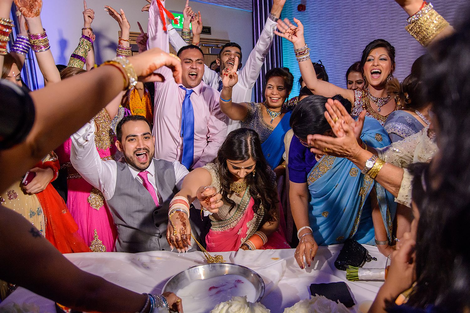 Energetic wedding guests dancing and celebrating with their hands raised in excitement at a reception party.