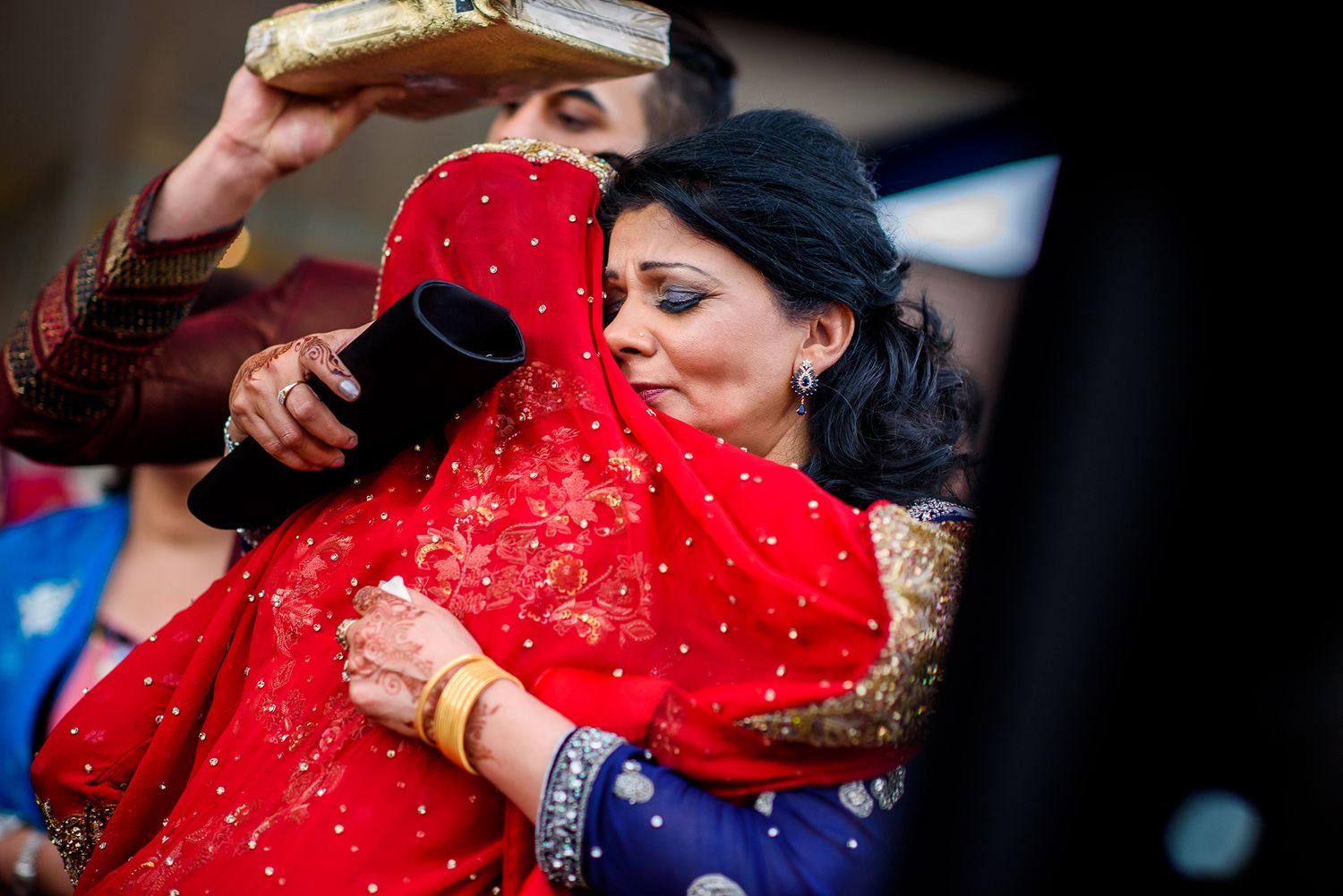 Detailed view of a red dupatta with intricate gold embellishments during an Indian wedding ceremony.