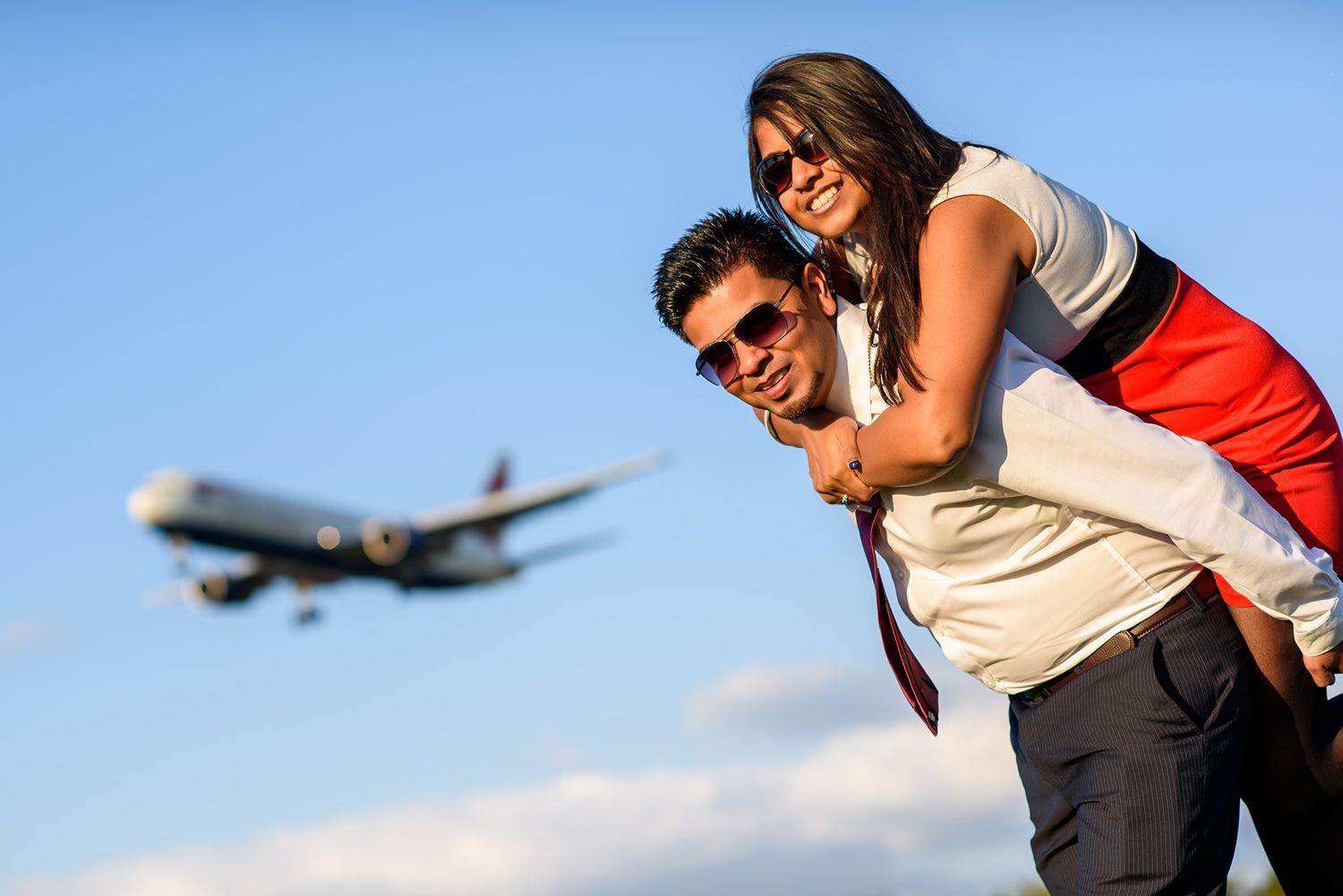 A joyful piggyback ride with an airplane flying overhead in the background.