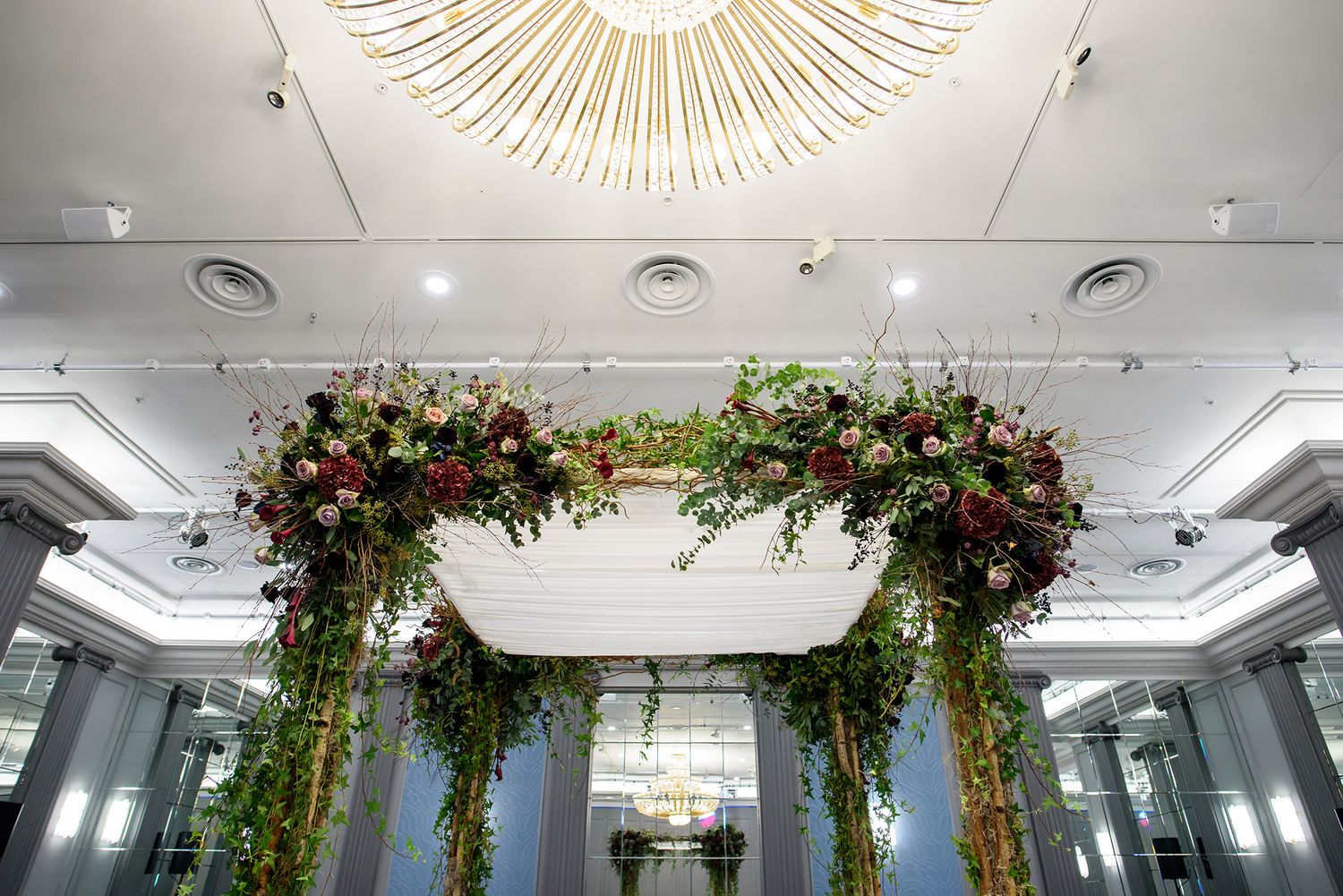 Stunning floral arch installation with red and green blooms under an ornate ceiling.