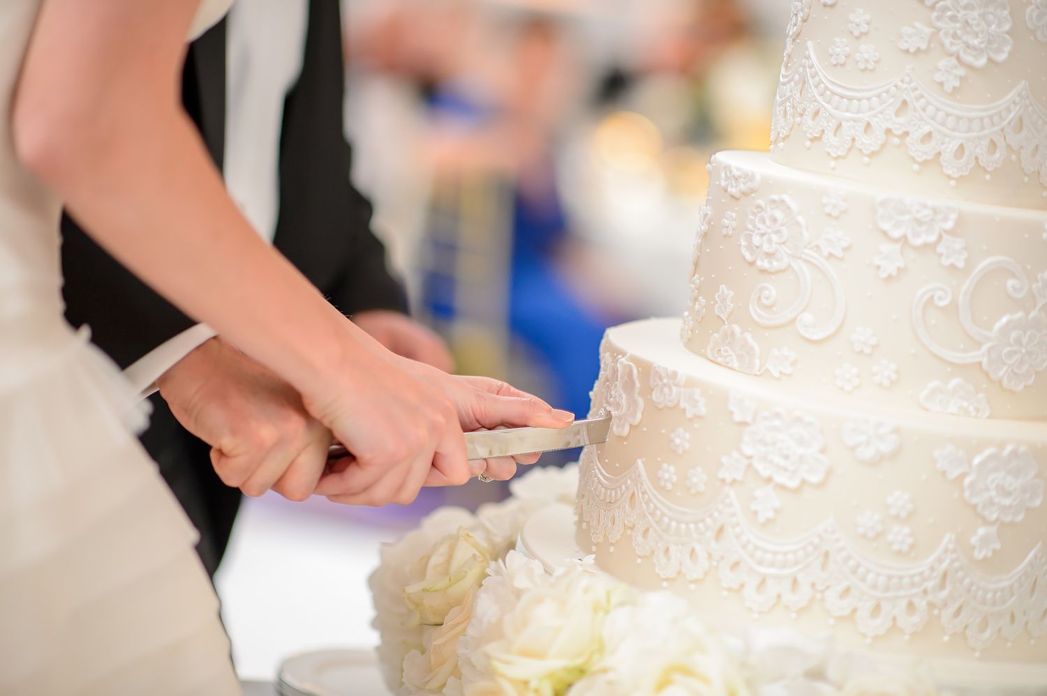 Wedding guests watch as a beautiful tiered white cake is cut during an elegant reception celebration.