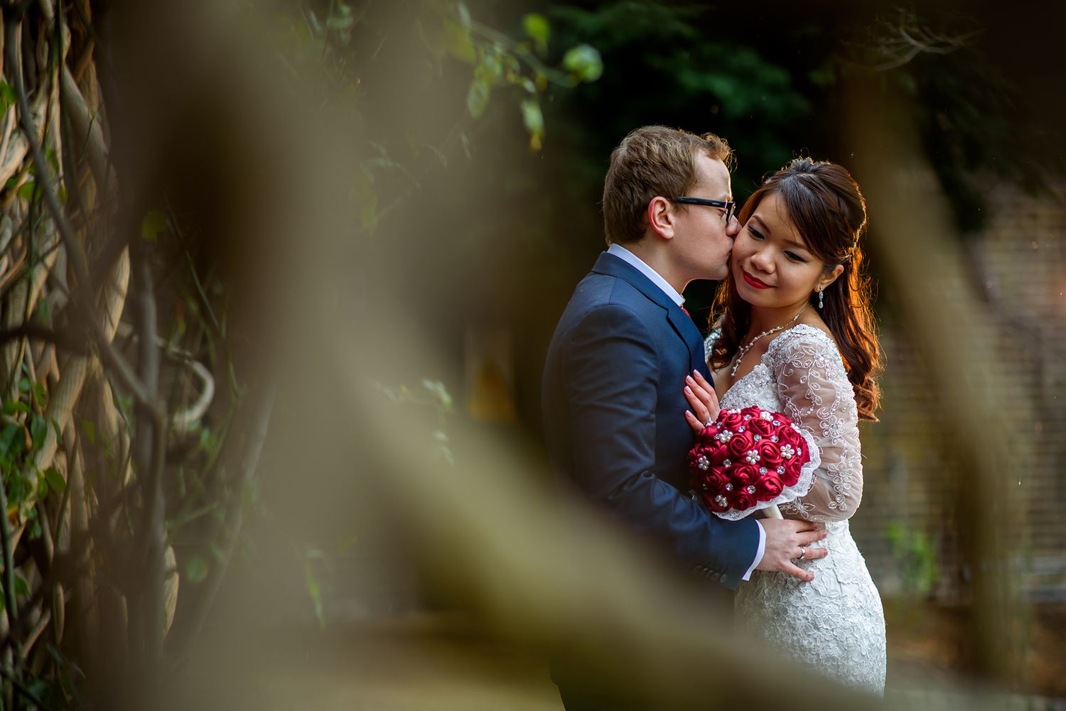 An intimate wedding photo taken through foliage with soft natural lighting.