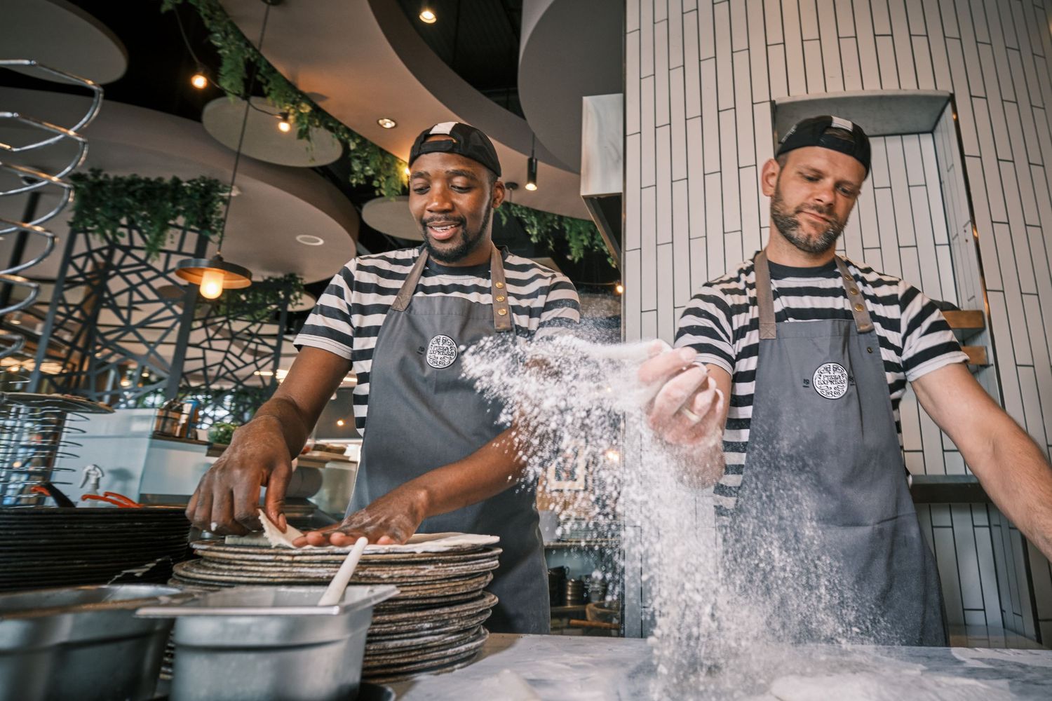 Chef tossing flour while preparing pizza dough in a professional kitchen.
