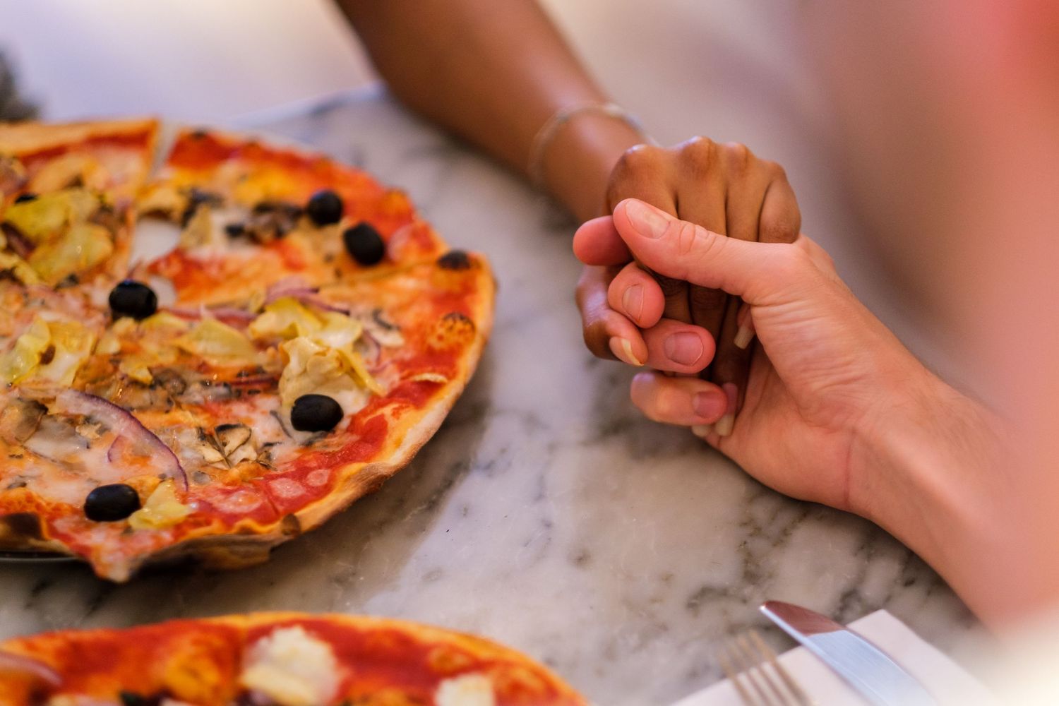 Close-up of fresh pizza with olives and toppings on marble counter.