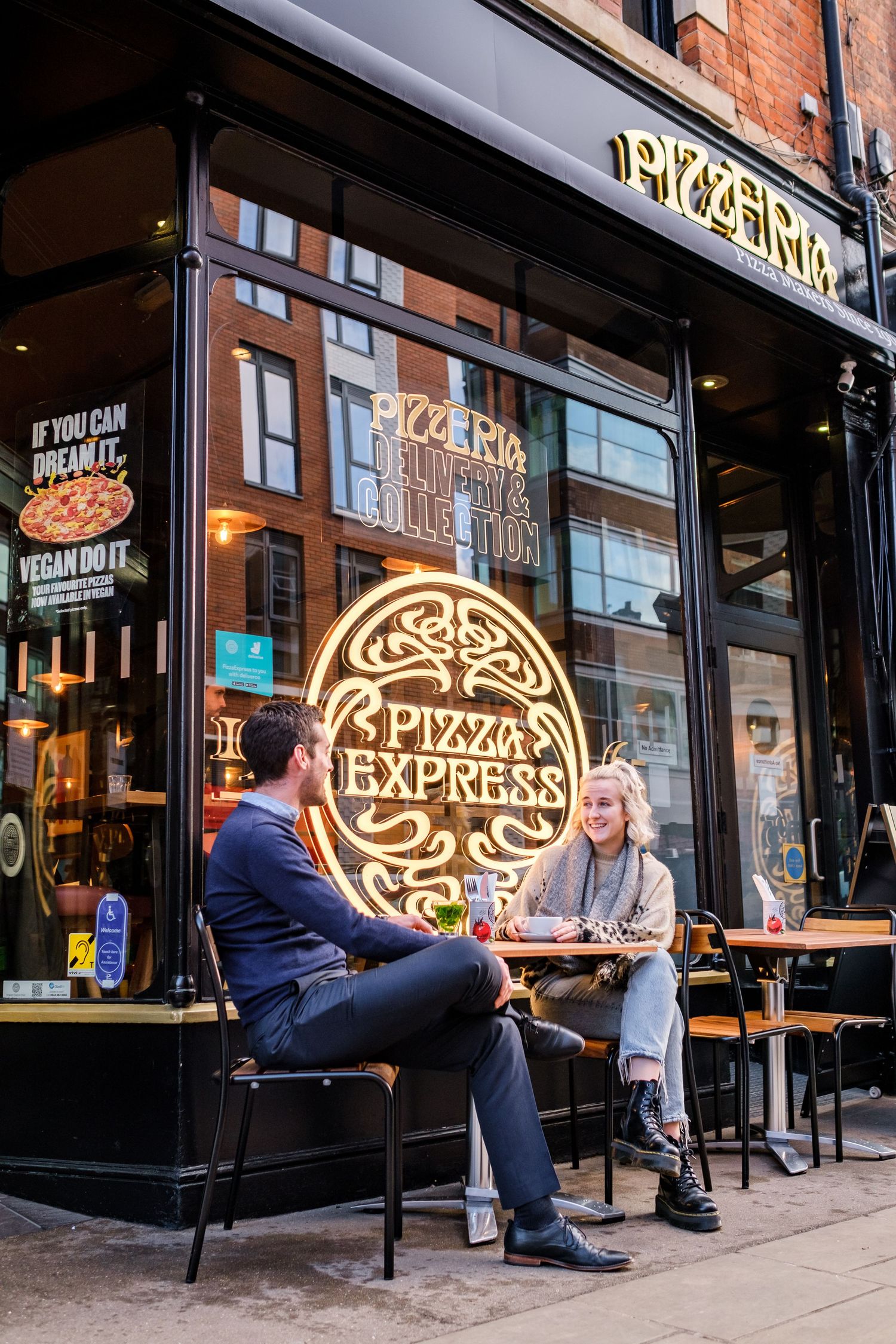 Pizza Express storefront with illuminated neon sign and outdoor seating area on a city street.