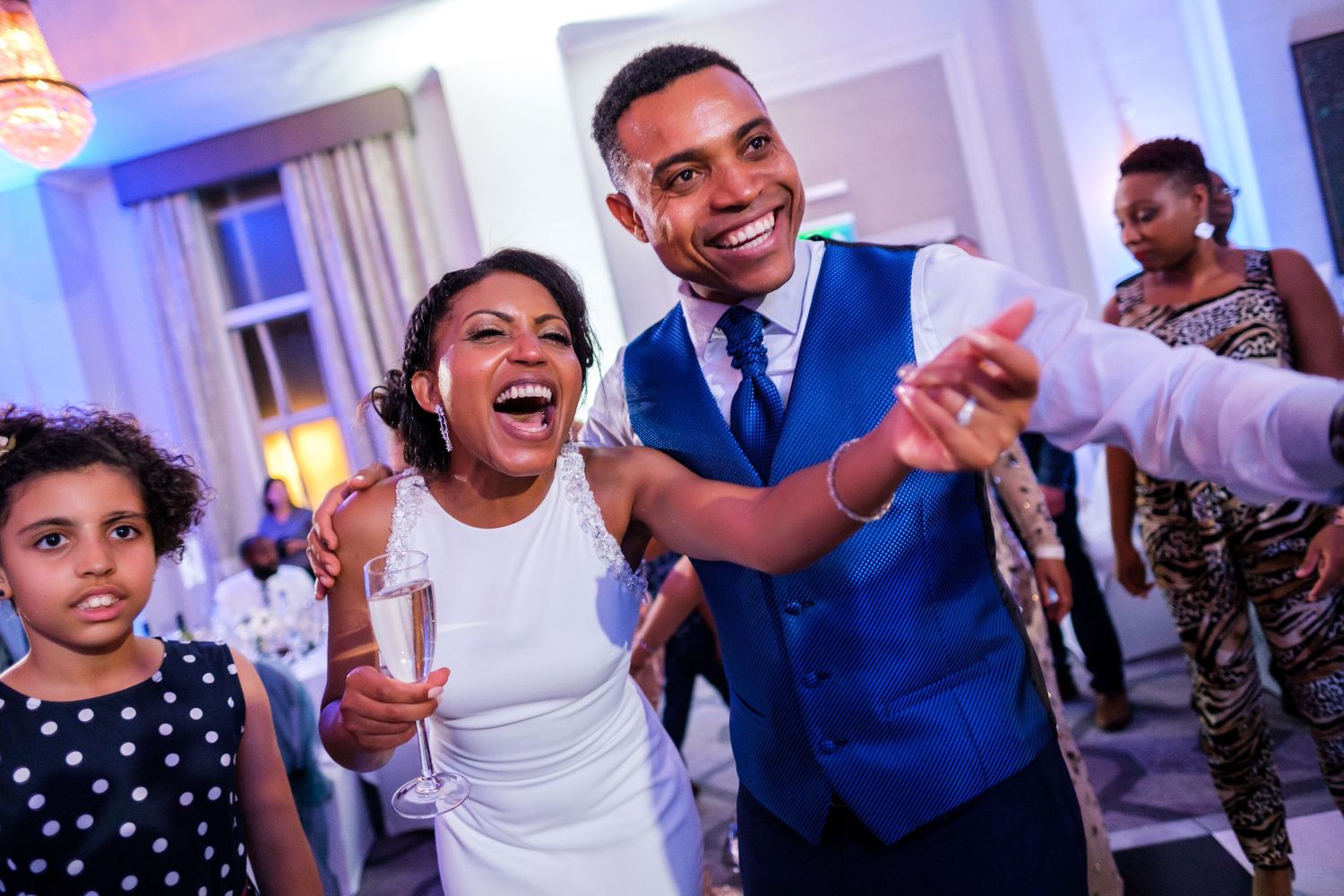 Wedding party dancing and celebrating with colorful purple uplighting in an elegant ballroom setting.