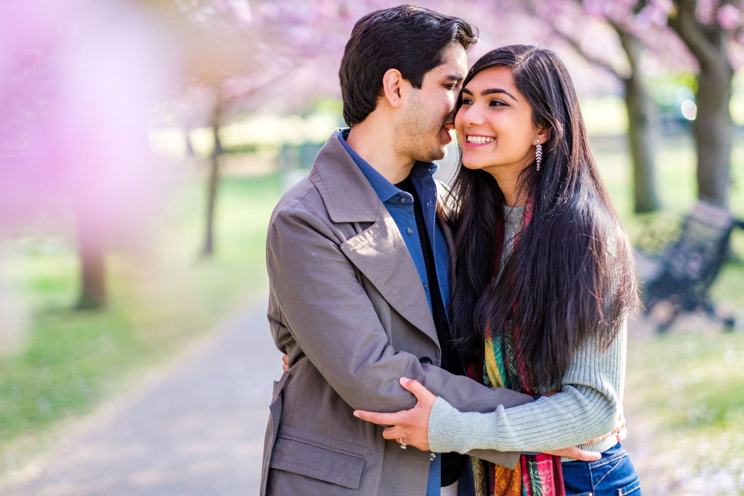 A couple shares romantic moments in a park during springtime with cherry blossoms blooming in the background.