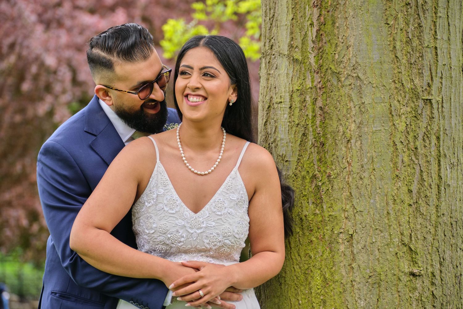 A couple shares tender moments during a romantic outdoor photo session among pink cherry blossoms and trees.