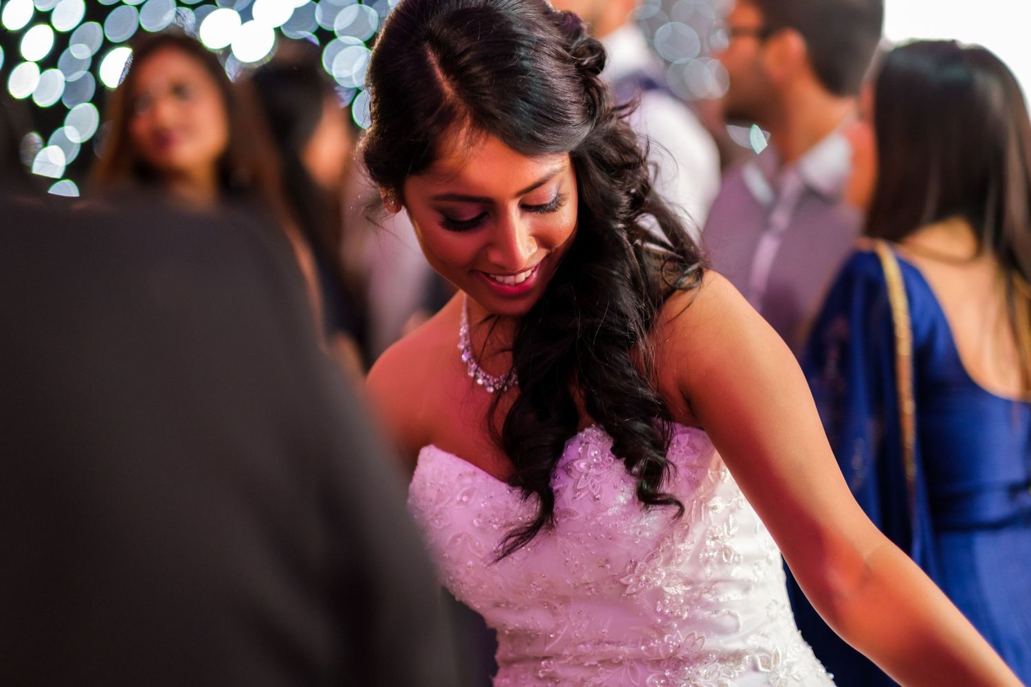 Bride in a pink dress dances during an evening wedding reception with bokeh lights in background.