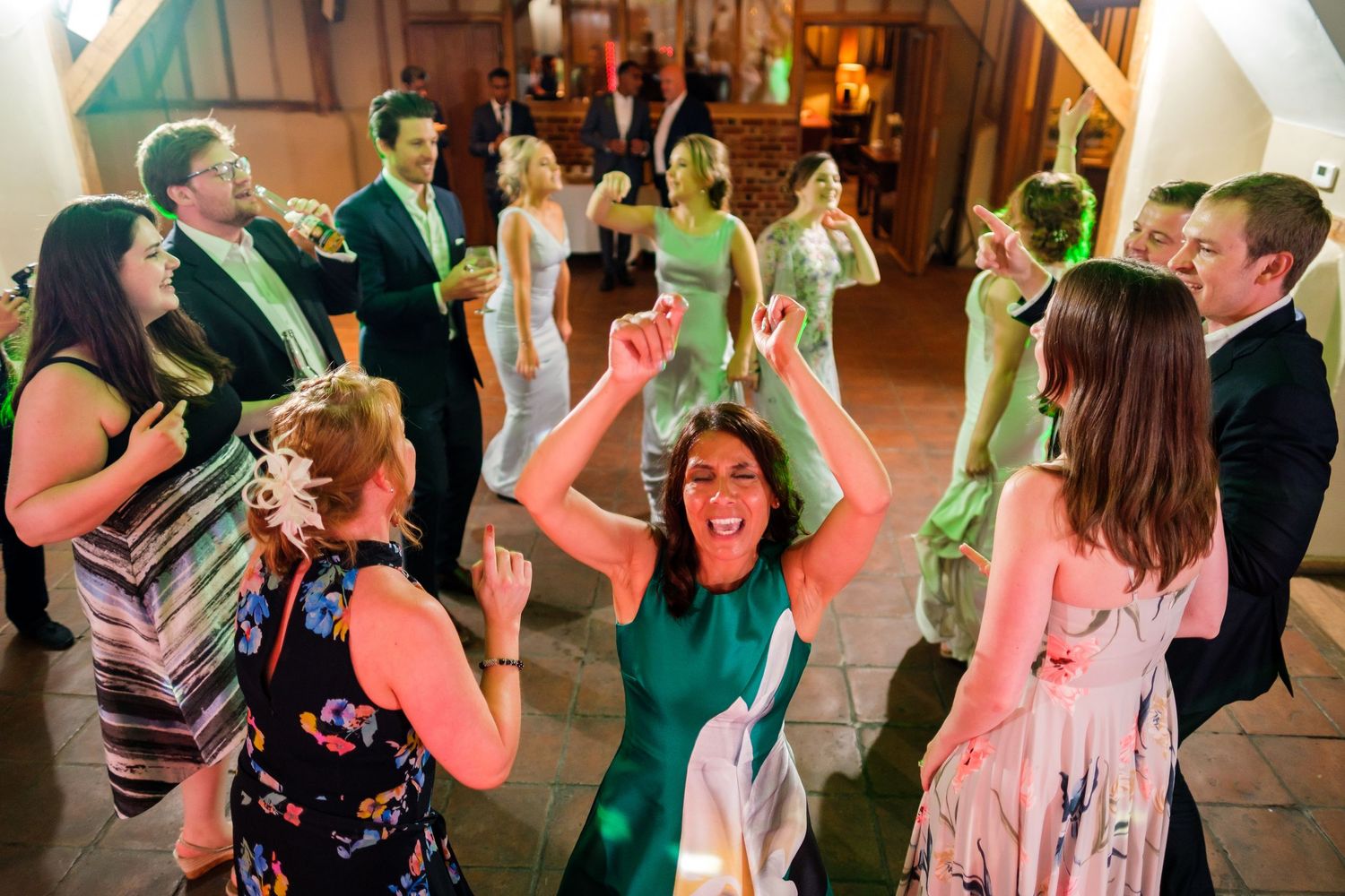 Energetic party crowd dances and celebrates at a wedding reception with dynamic lighting effects.