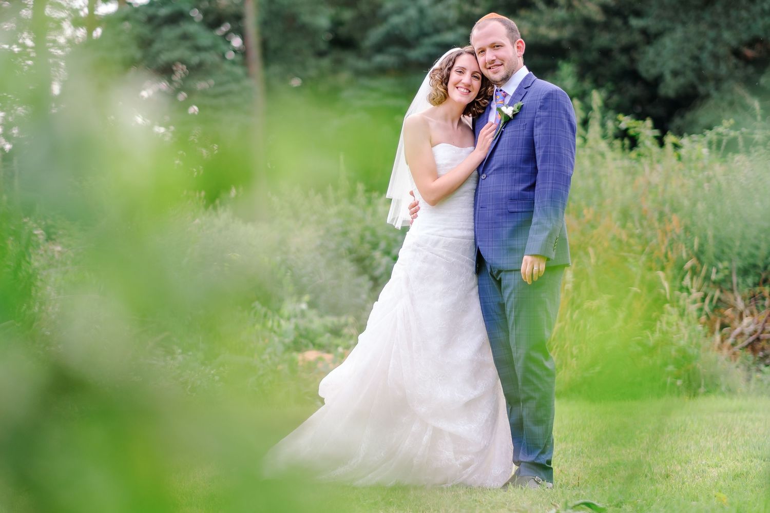 Romantic wedding portrait in tall grass with soft natural lighting and dreamy atmosphere.