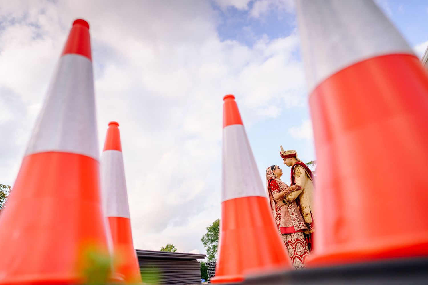 Creative wedding photo composition with orange traffic cones against cloudy sky.