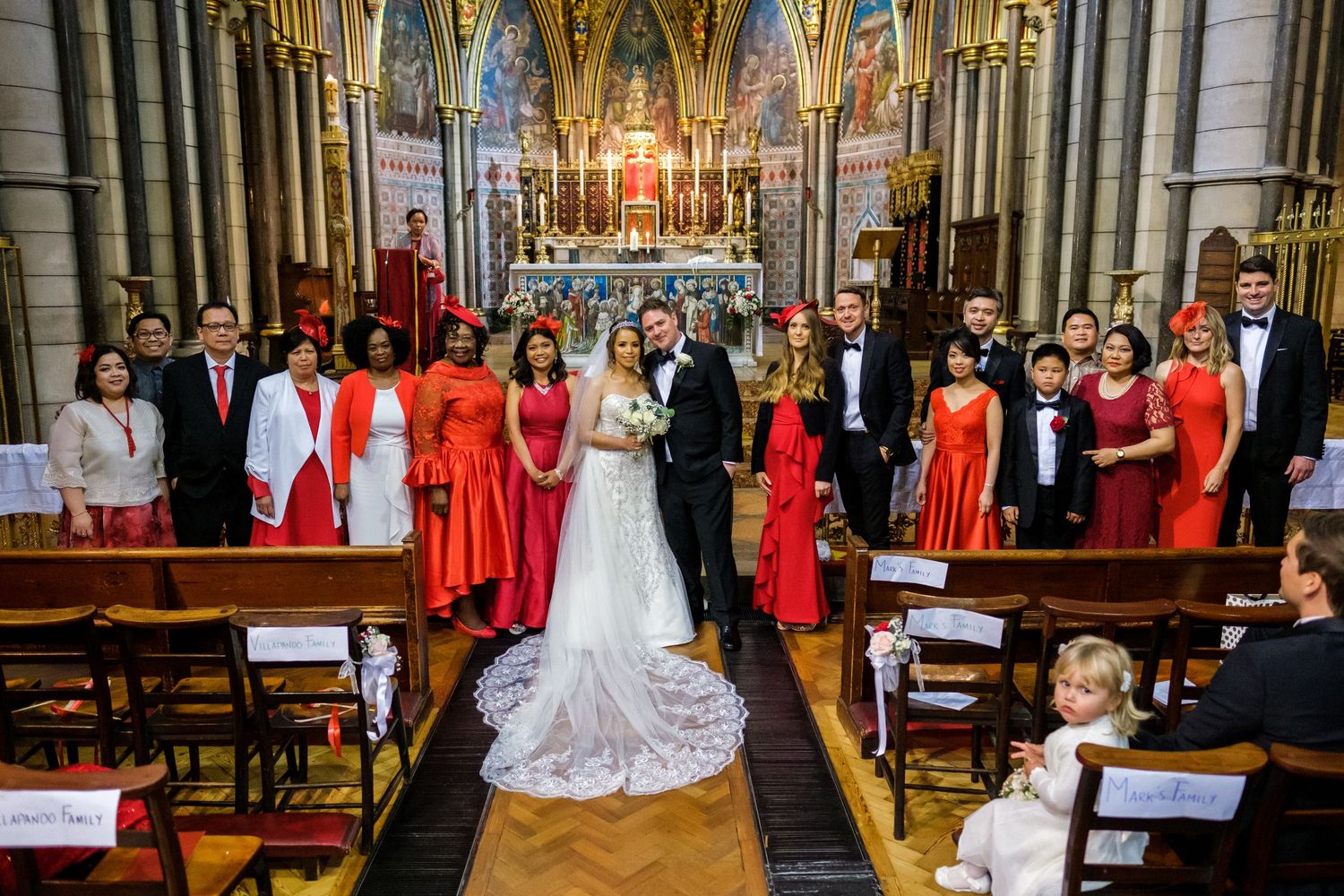 Wedding party gathered in majestic cathedral with gothic architecture and stained glass windows.