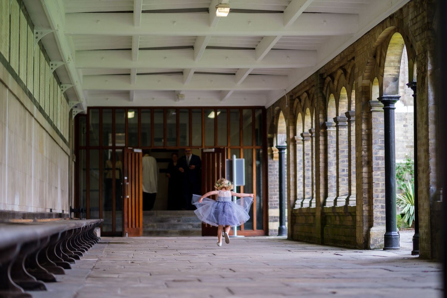 Long empty corridor with arched windows and stone columns in an abandoned building shows architectural decay.