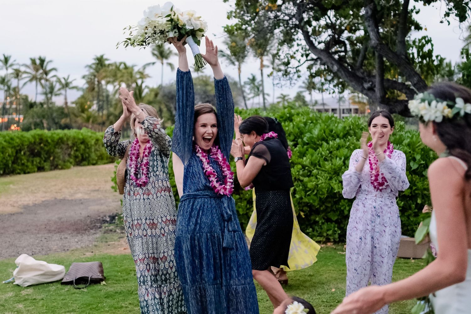Wedding party celebrates outdoors with joyful dancing and laughter under palm trees at a tropical venue.