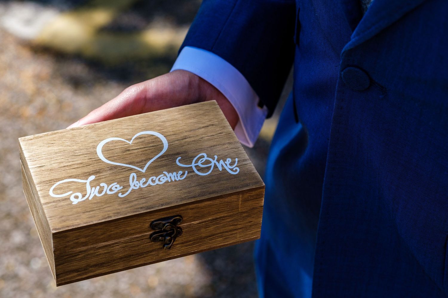 Rustic wooden ring box with heart detail and engraving sits on display at wedding ceremony.