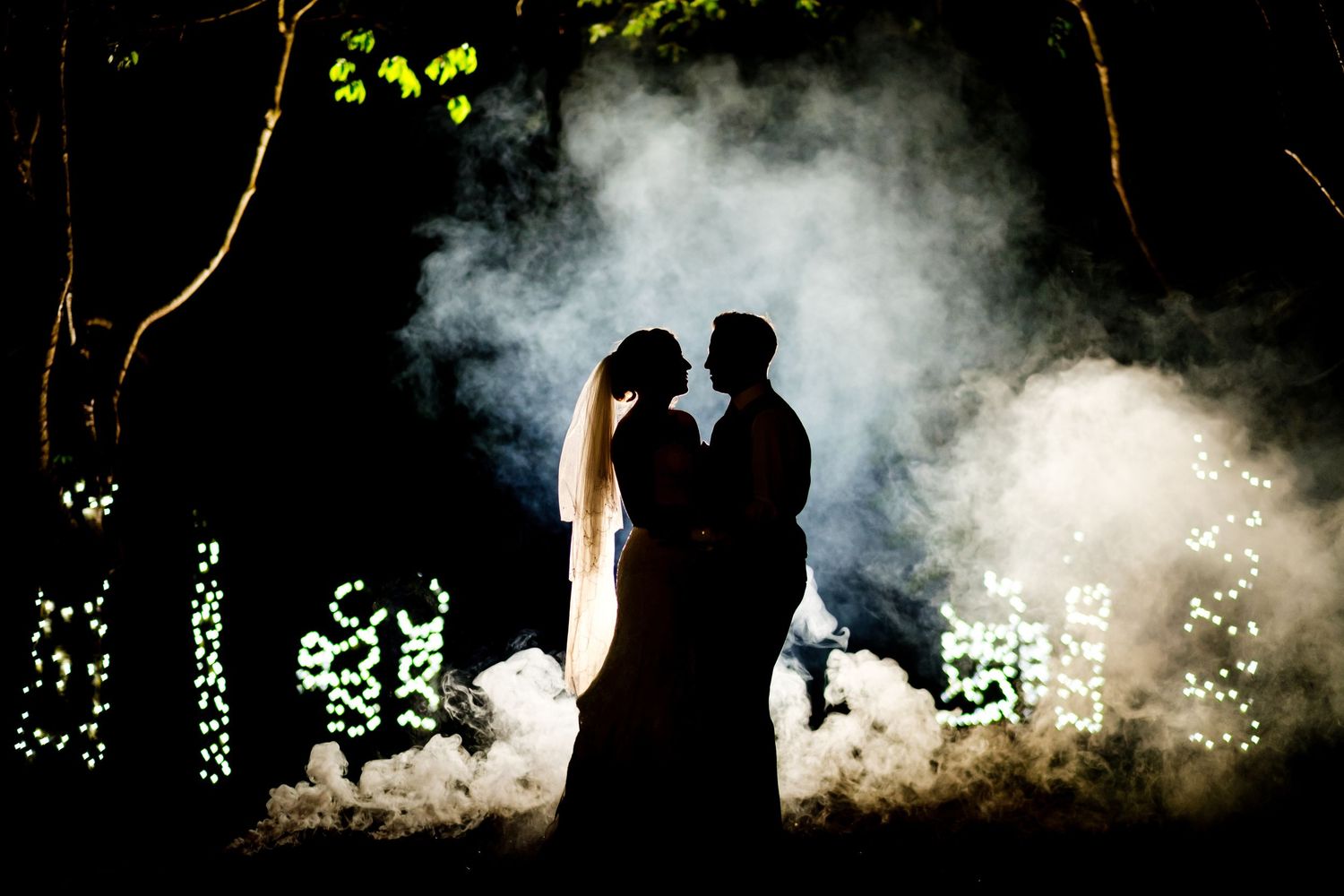 Silhouetted wedding couple against atmospheric smoke and lighting.