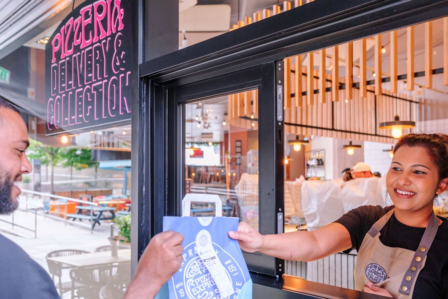 Restaurant worker in apron serving customer through takeout window.