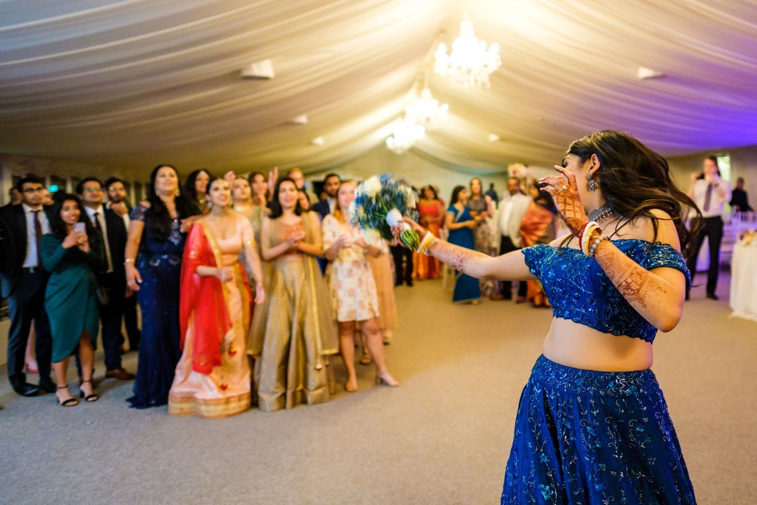 Wedding reception dance party in decorated marquee tent with chandelier and mood lighting.