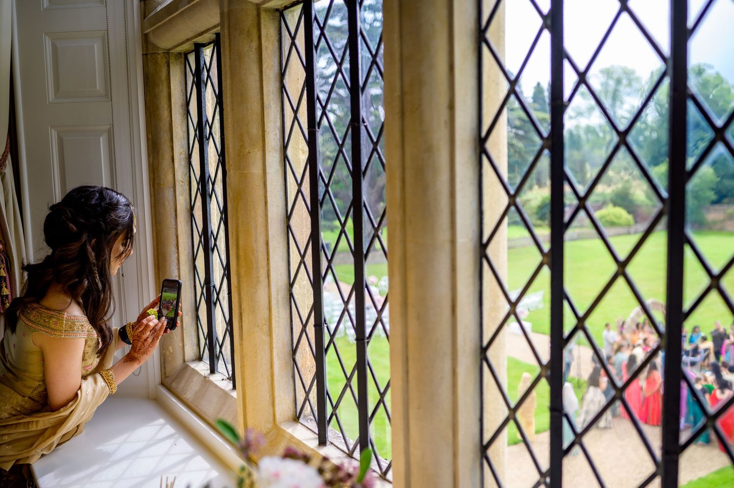 Someone in a yellow dress looks through a diamond-patterned window at a crowd gathered outside on a sunny day.
