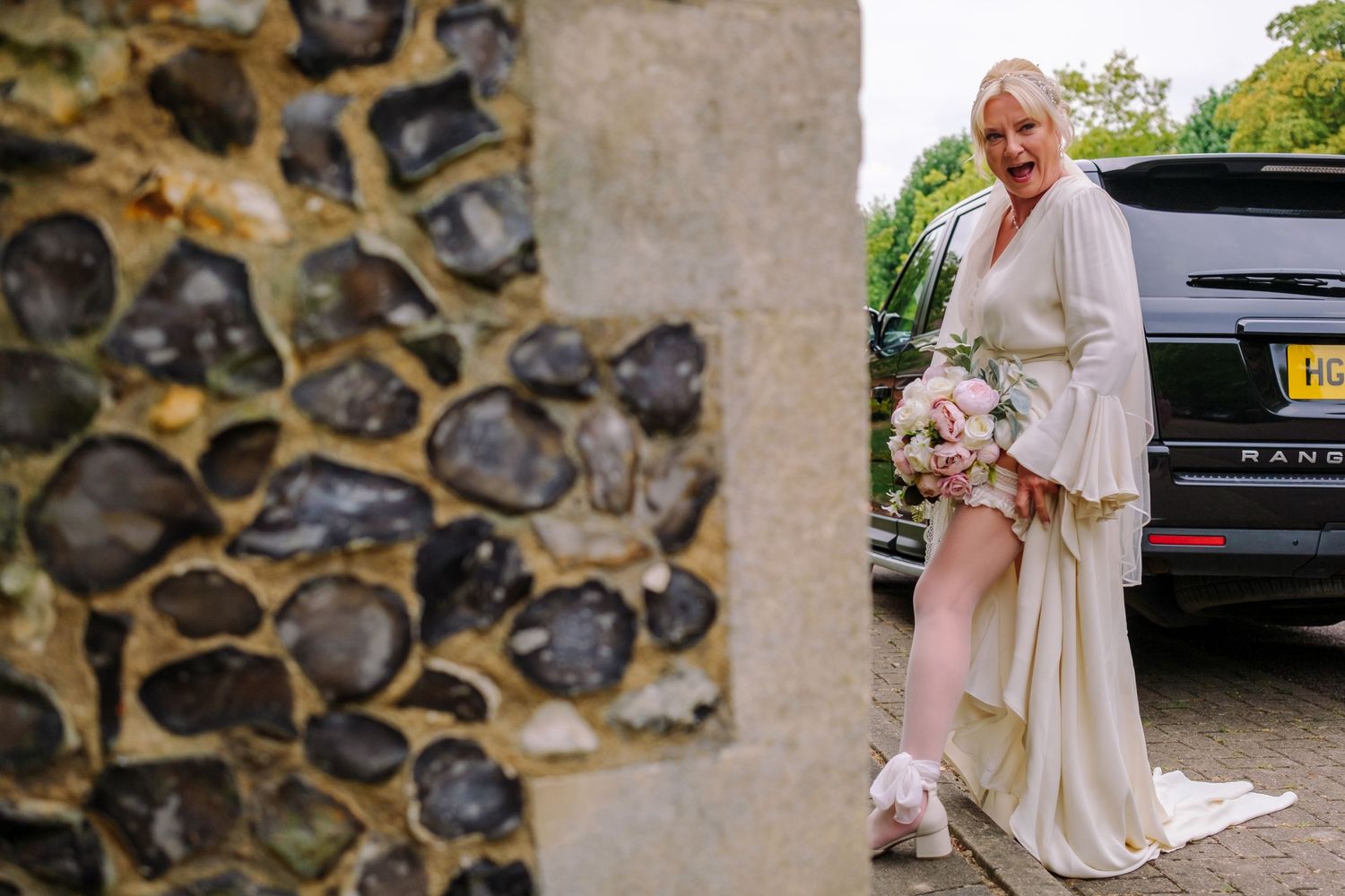 Wedding guests gather outdoors near a stone wall during a sunny celebration.