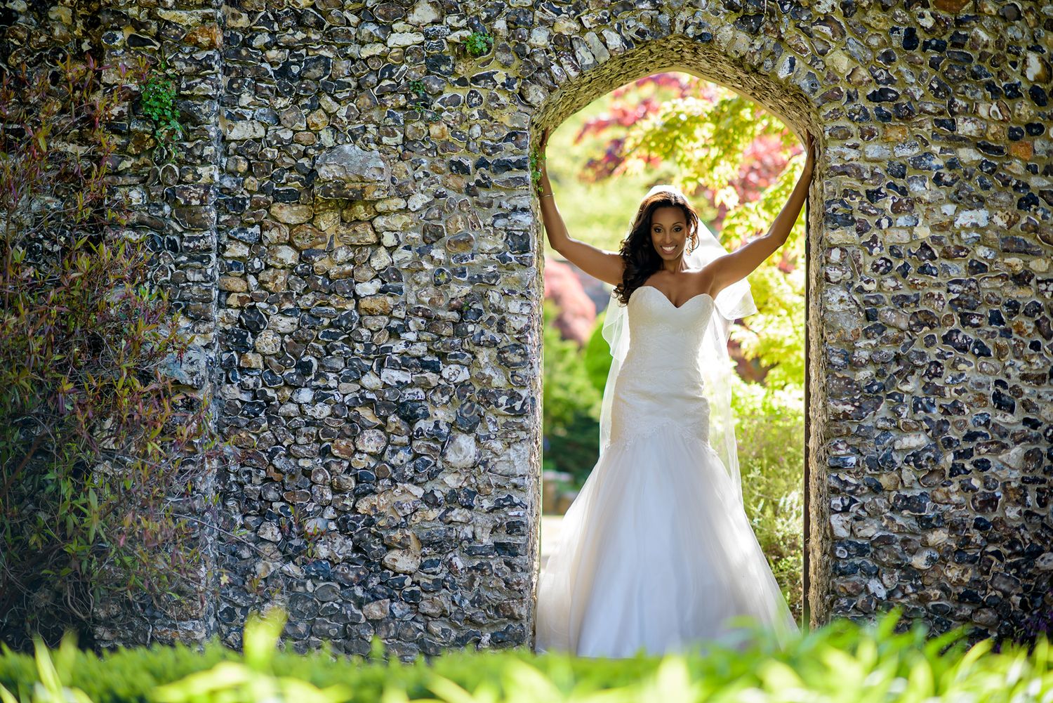 Bridal portraits against rustic stone wall archway in garden setting.