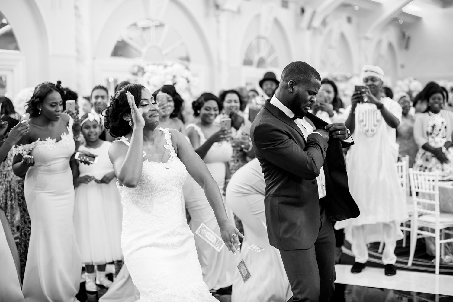 Wedding guests dancing and celebrating in an elegant white reception hall.