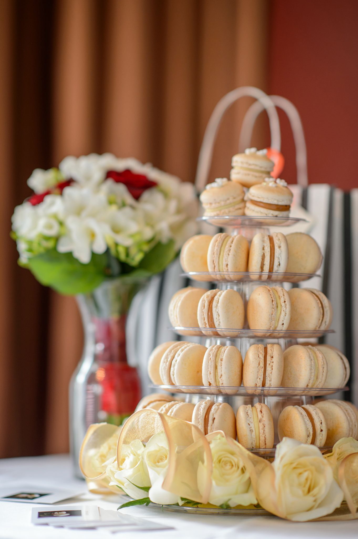 Elegant tiered display of macarons with white roses at a wedding reception.