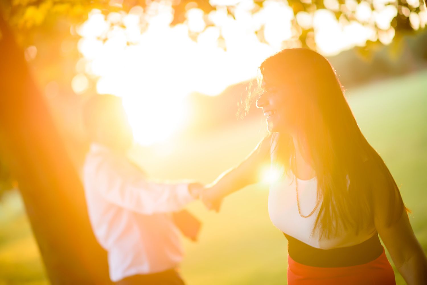 A silhouetted couple holds hands during a golden sunset in a park.