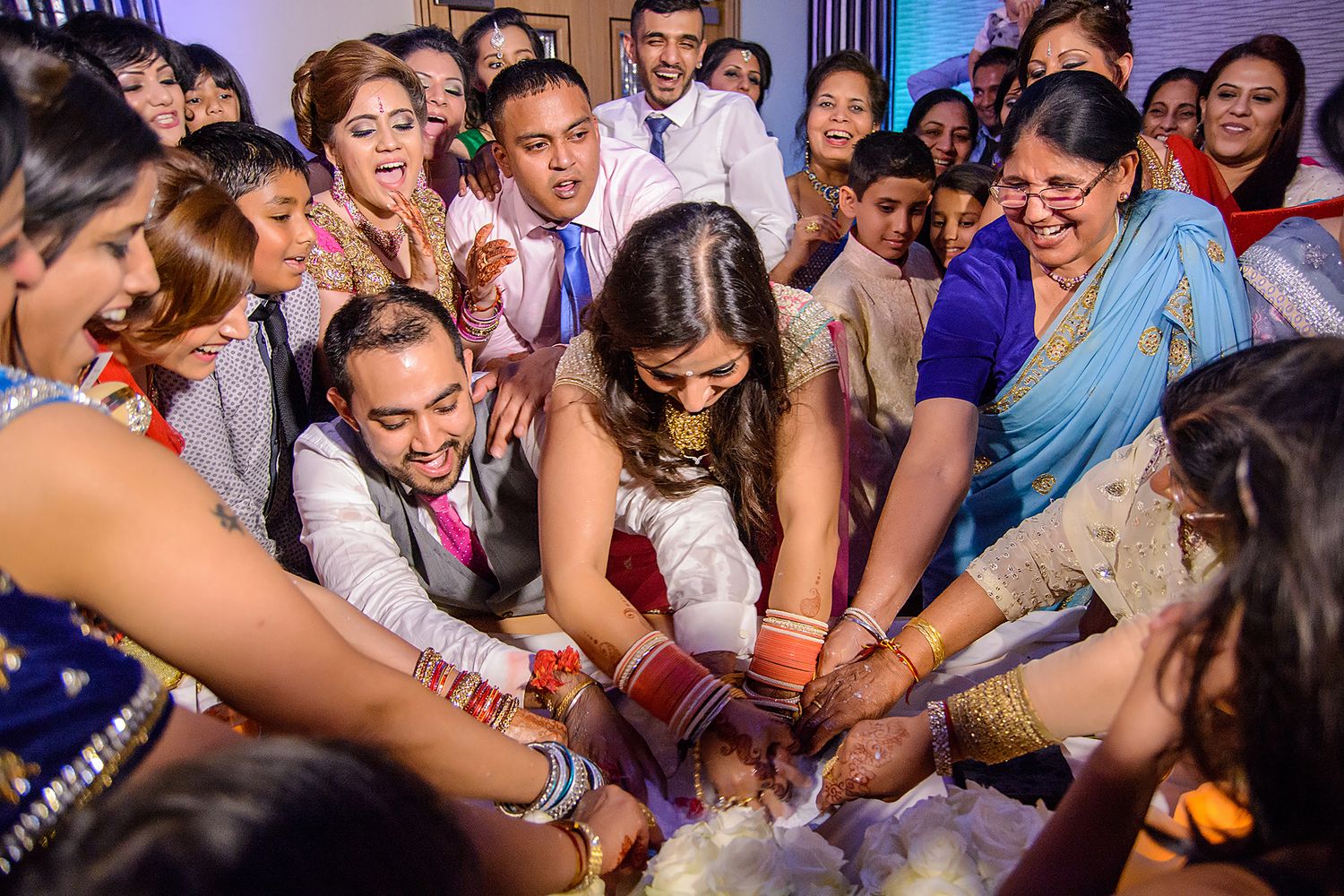 Wedding celebration showing guests gathered in a circle reaching toward the center during a party game.