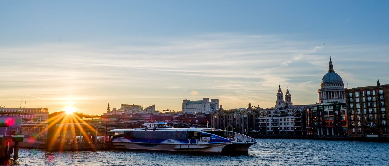 Panoramic cityscape at sunset with sun rays bursting over water and buildings.