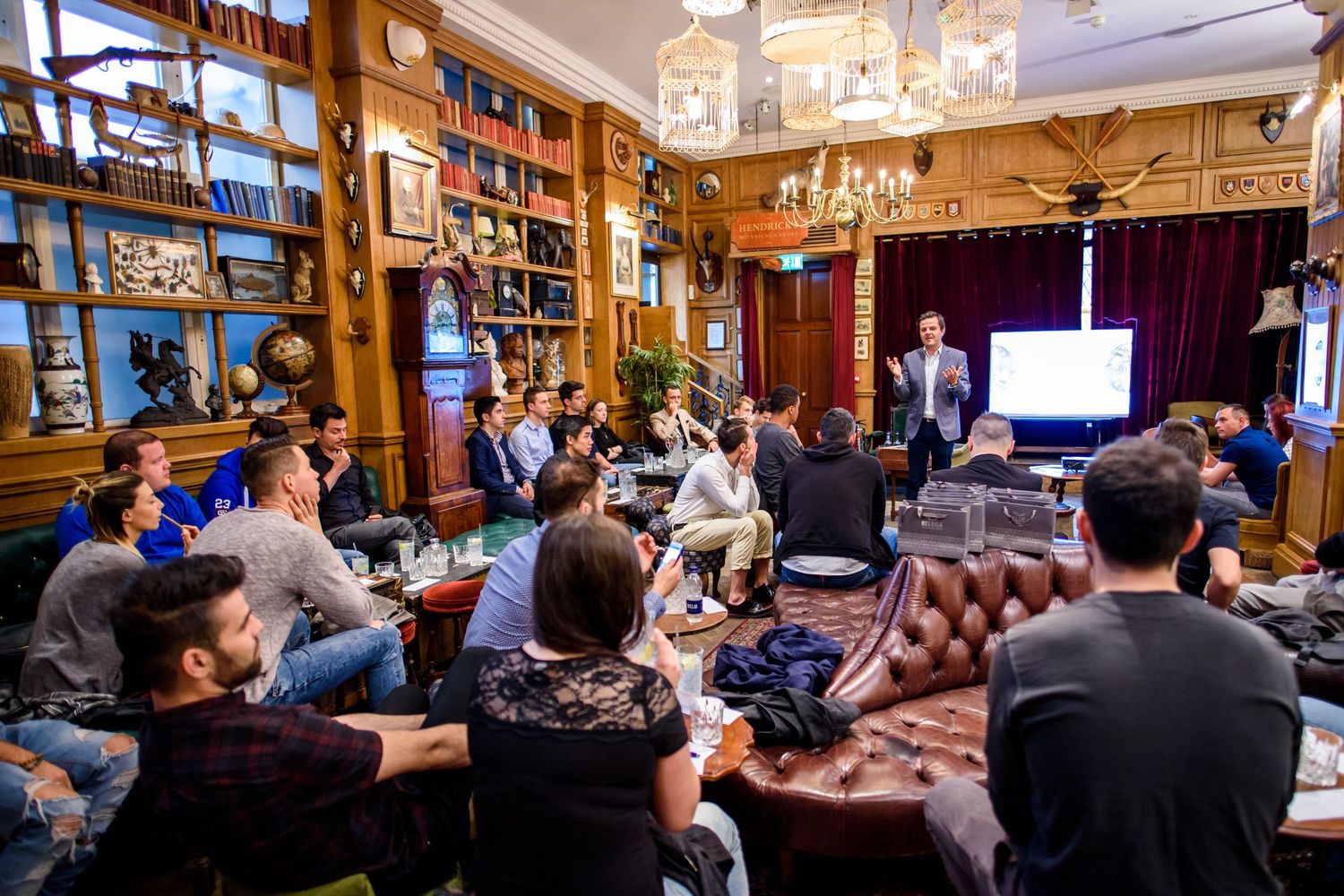 People gathered in a cozy library-style room with leather seating and warm lighting for a presentation or meeting.