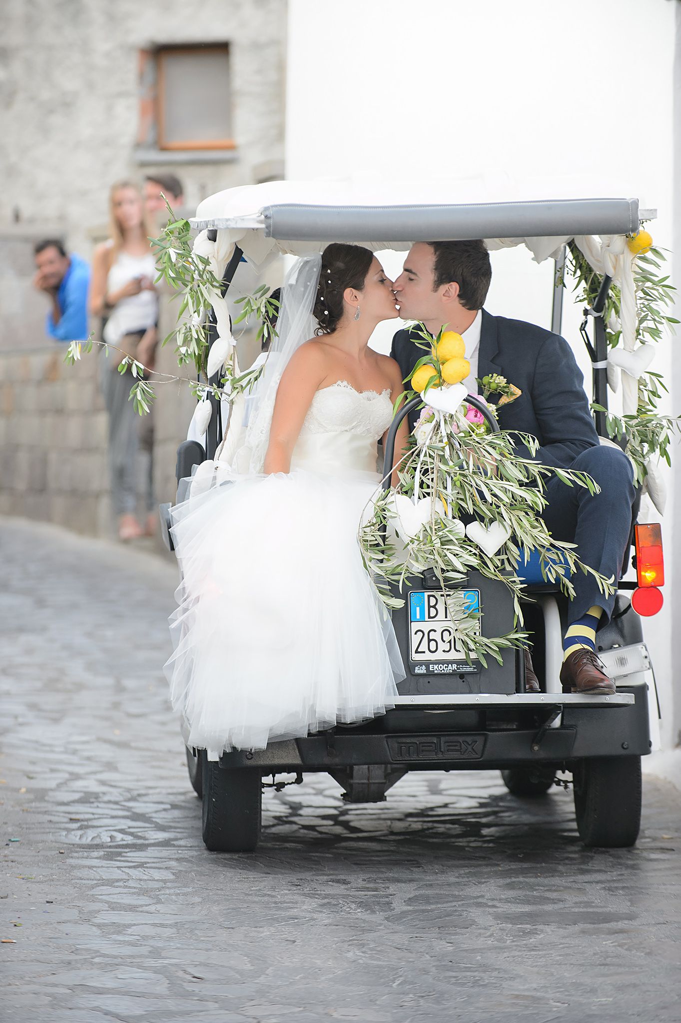 Wedding couple riding in a decorated golf cart on cobblestone streets.