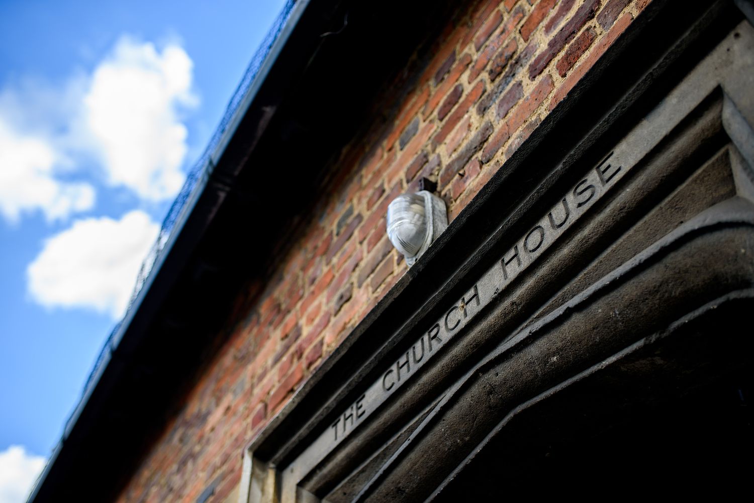 An architectural detail of a brick building with a vintage lamp against a blue sky.