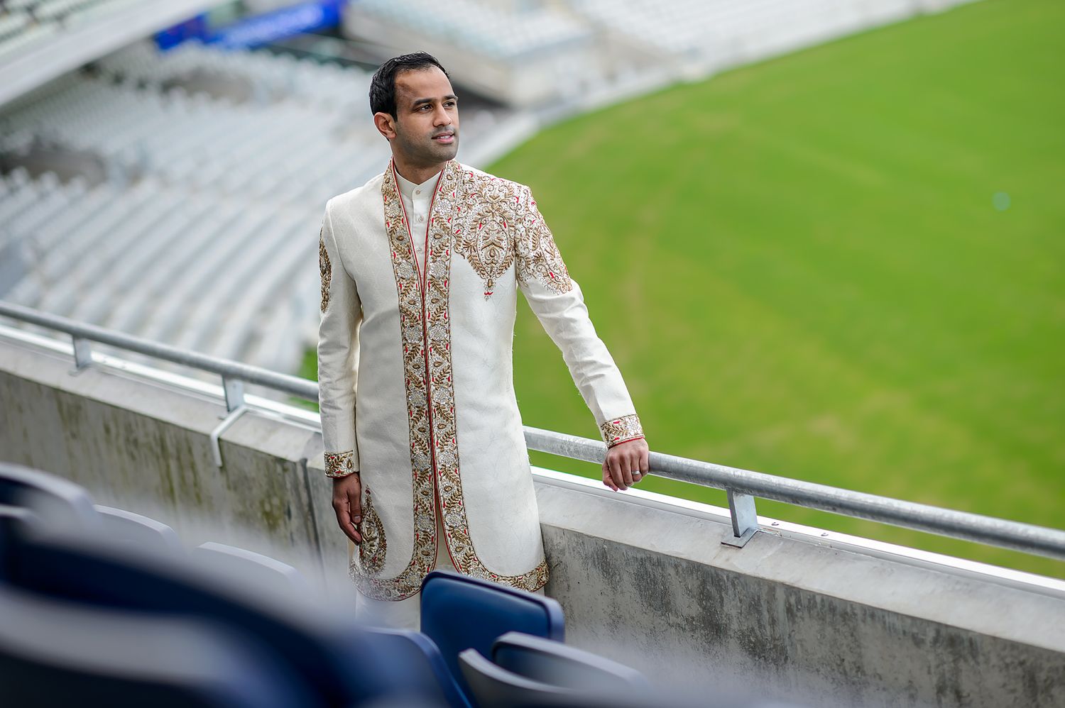 Person in cream colored formal attire standing against outdoor stadium railing.