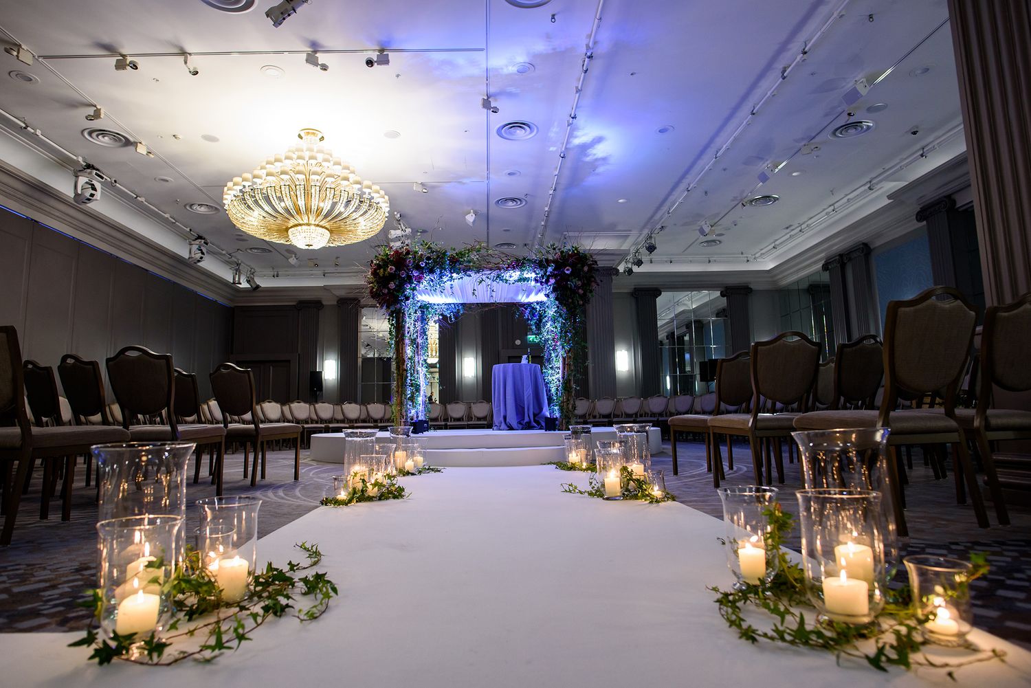Romantic wedding ceremony setup with candlelit aisle and elegant chandelier lighting.