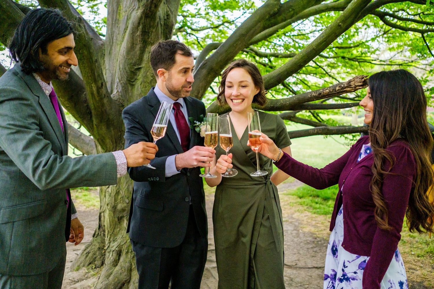 People celebrating with drinks and snacks beneath a large tree at a garden party.