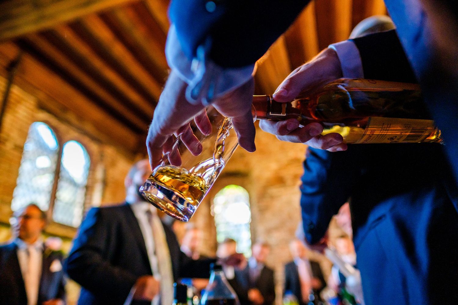 Whiskey being poured into glasses during a celebratory toast at an indoor venue.