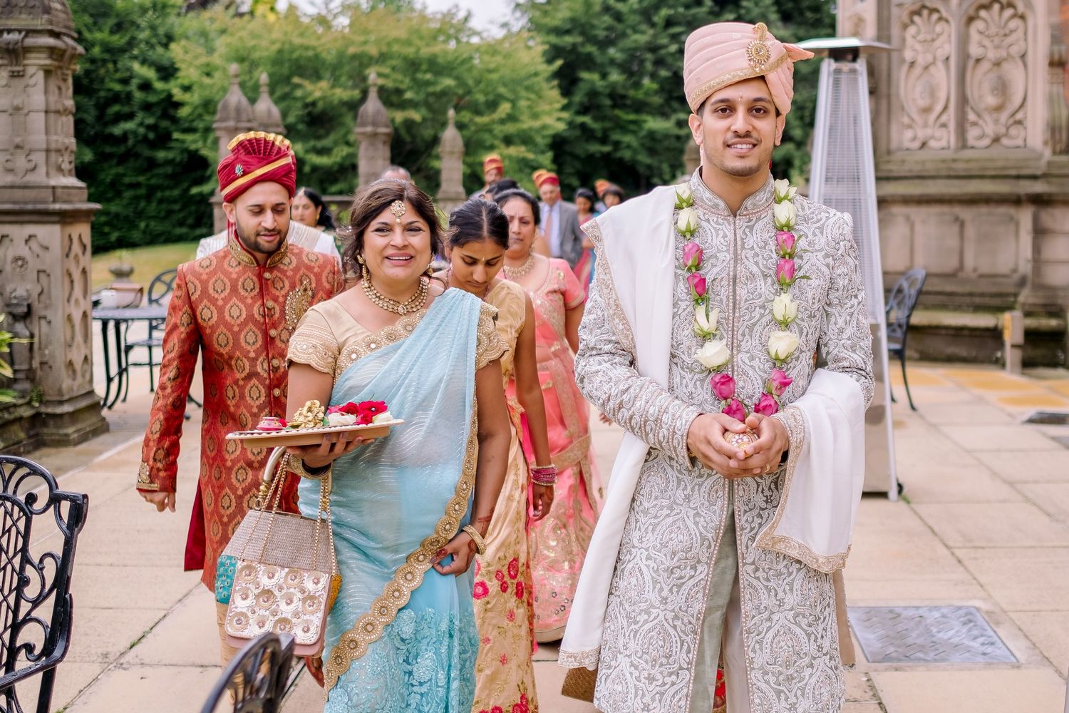 Wedding party in traditional South Asian attire walking outside historic stone building.