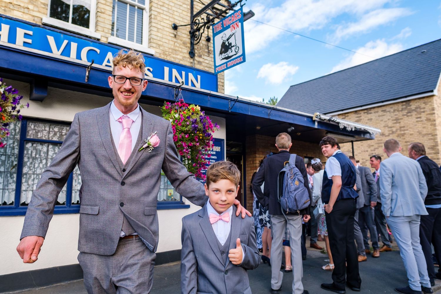 Wedding guests mingle and celebrate outside a historic stone building on a sunny day.