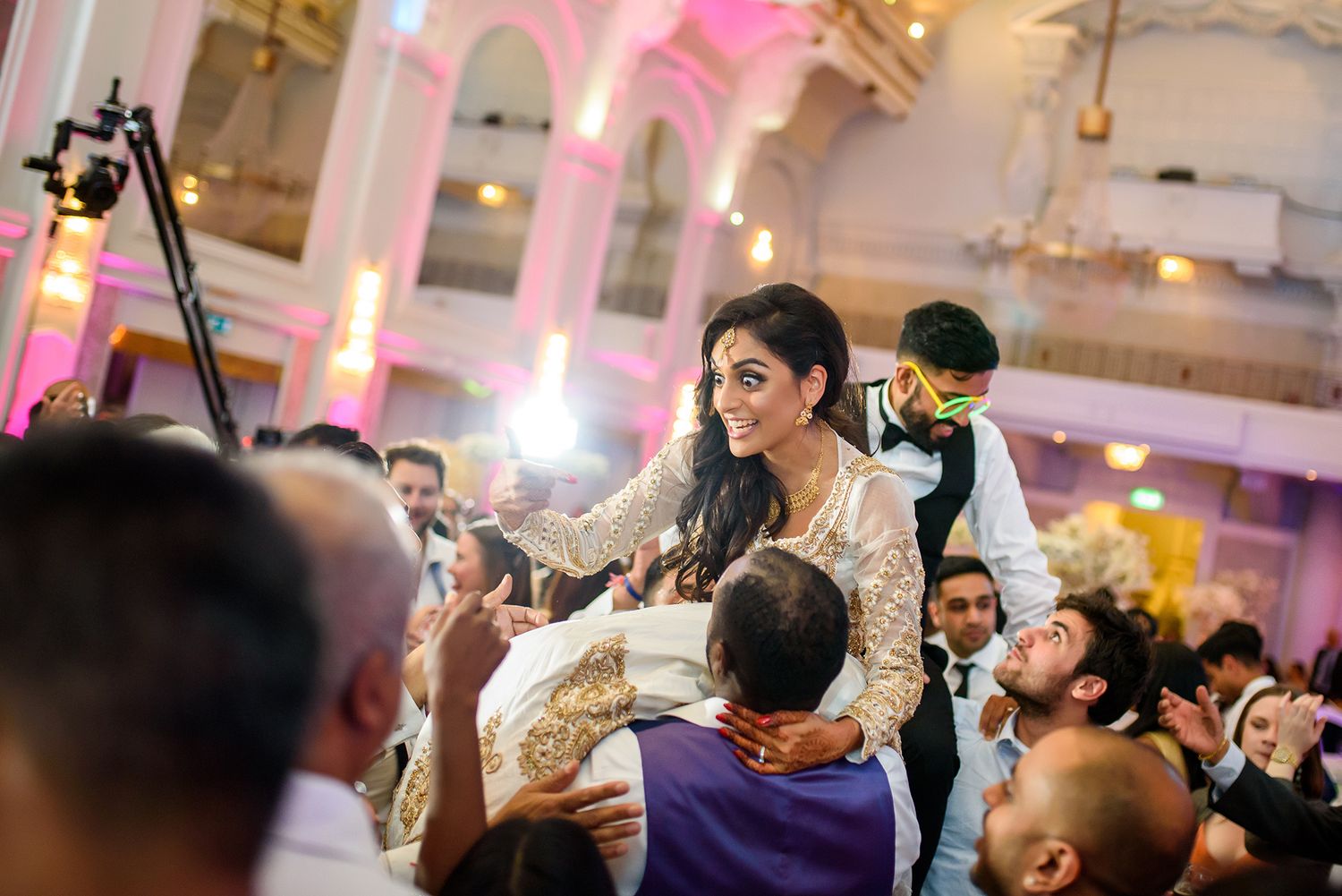 Wedding guests dance and celebrate in an elegant ballroom with ornate architectural details.