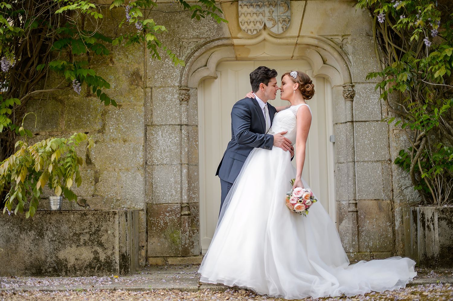Wedding couple shares intimate moments against historic stone wall covered in vines.